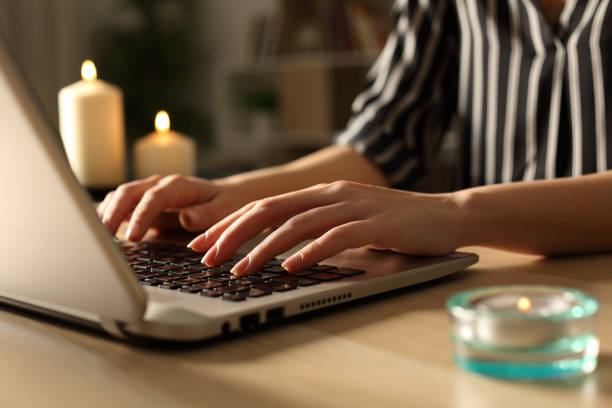 girl working on laptop on power outage with candles sitting on a desk at home in the night